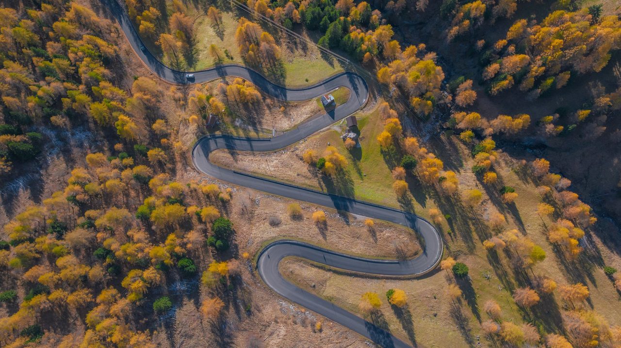 Una strada di montagna a tornanti fra i larici d'autunno, vista dall'alto